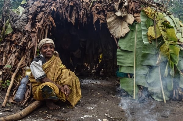 Indigenous Woman sitting next to a hut. 