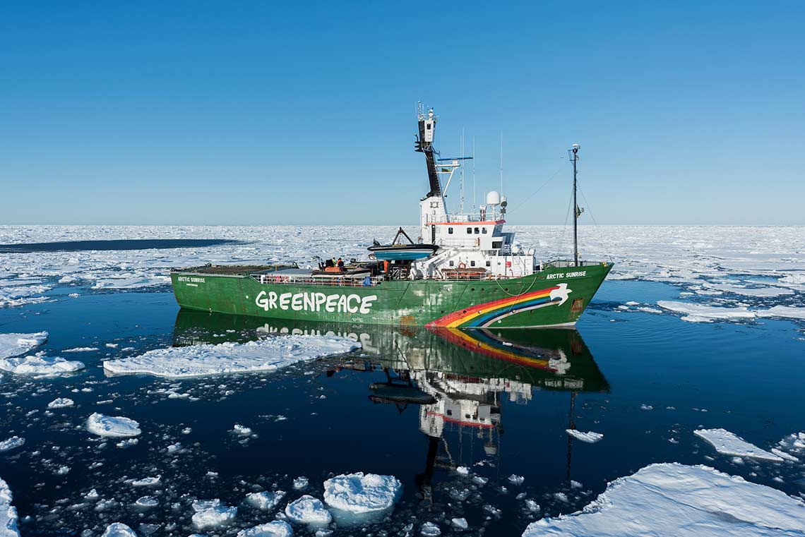 A dark green Greenpeace ship floats surrounded by ice in the Greenland Sea