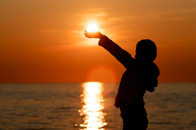 A silhouette of a child holding the sun over the ocean A silhouette of a child holding the sun over the ocean