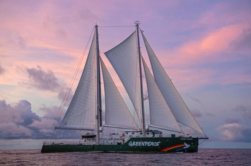 The Rainbow Warrior under sail in the Pacific with pink skies