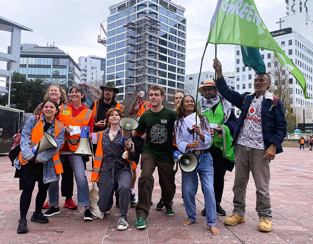 A group of Greenpeace volunteers posing and smiling before a Greenpeace march. They hold megaphones and Greenpeace flags.
