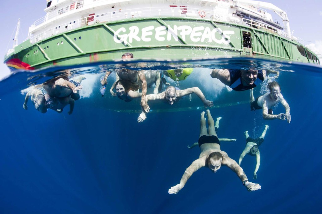 Greenpeace crew pose underwater next to the side of the Rainbow Warrior
