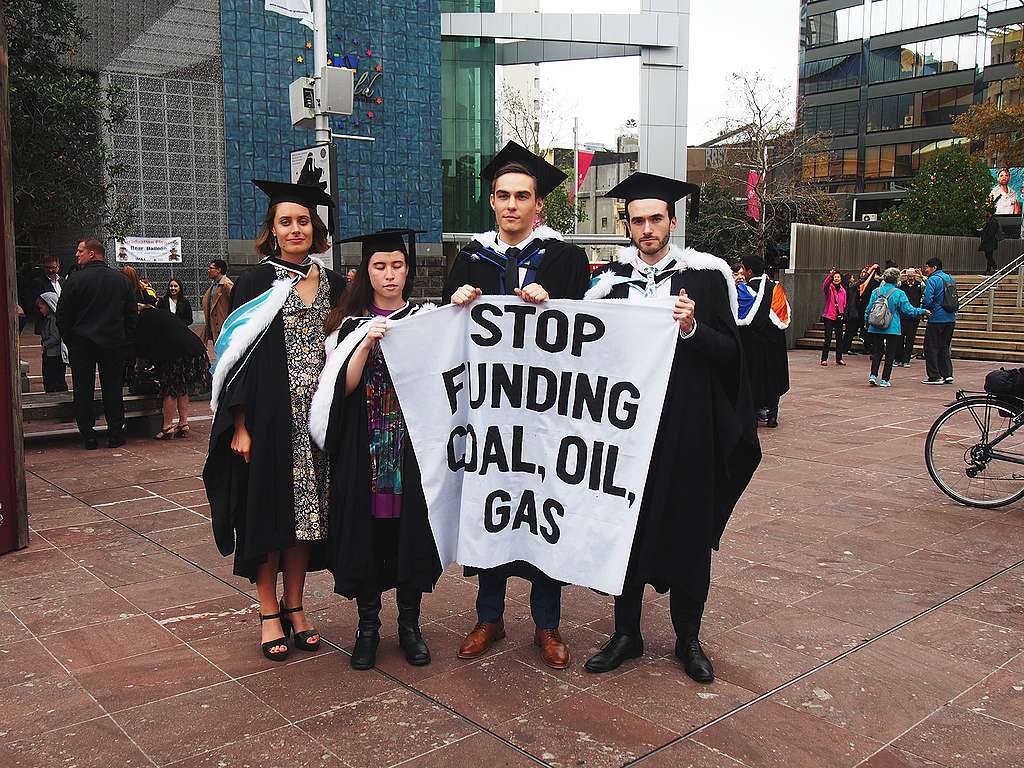 Aine and three other Fossil Free UoA members outside their graduation ceremony, wearing graduation robes and holding a banner that reads “Stop Funding Coal, Oil and Gas” – 2017