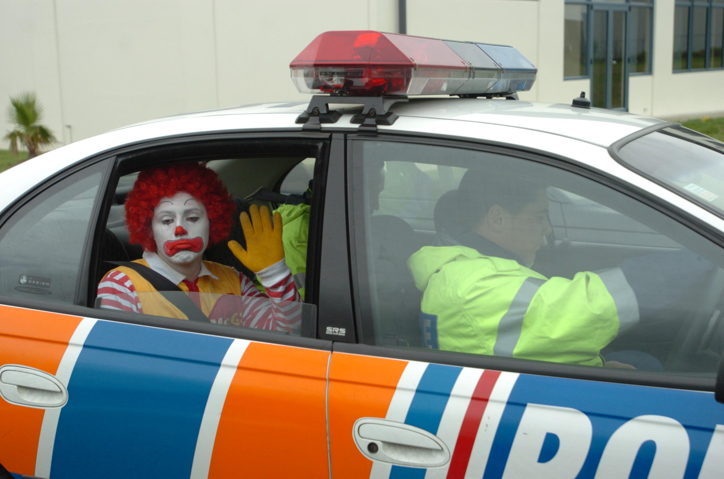 A Greenpeace activist dressed as Ronald McDonald waves sadly from the back off a cop car after getting arrested for locking himself to the gates of McDonald's South Auckland Distribution Centre