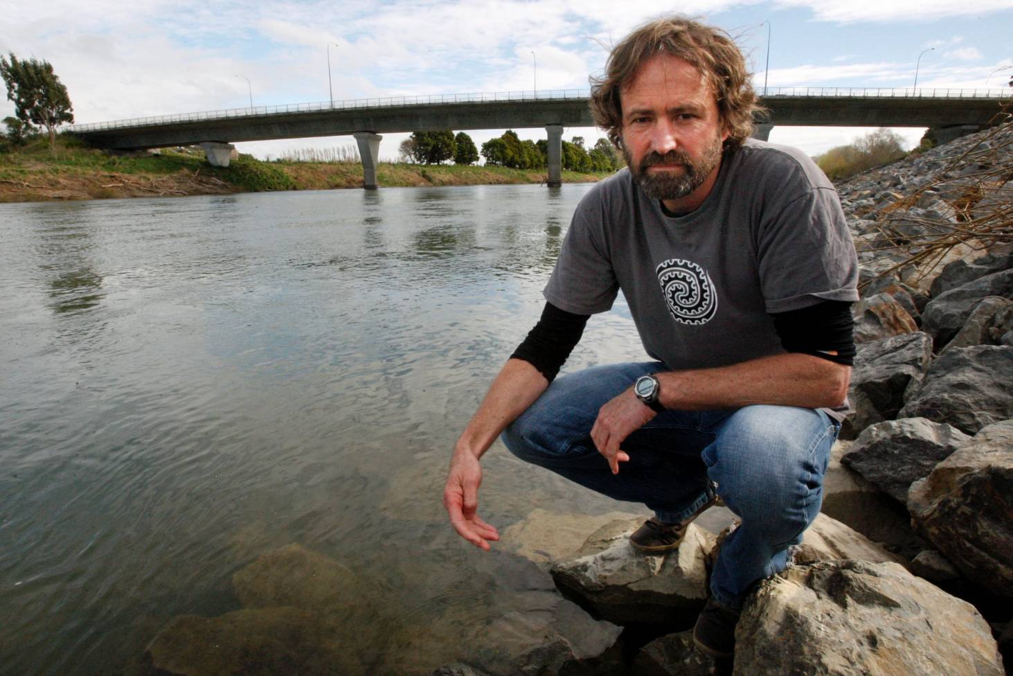 Mike Joy standing by a opaque river, looking serious