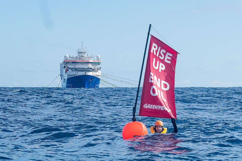 Russel Norman swimming with a buoy and banner that reads "Rise Up / End Oil" in front of seismic testing vessel Amazon Warrior. © Jason Blair / Greenpeace