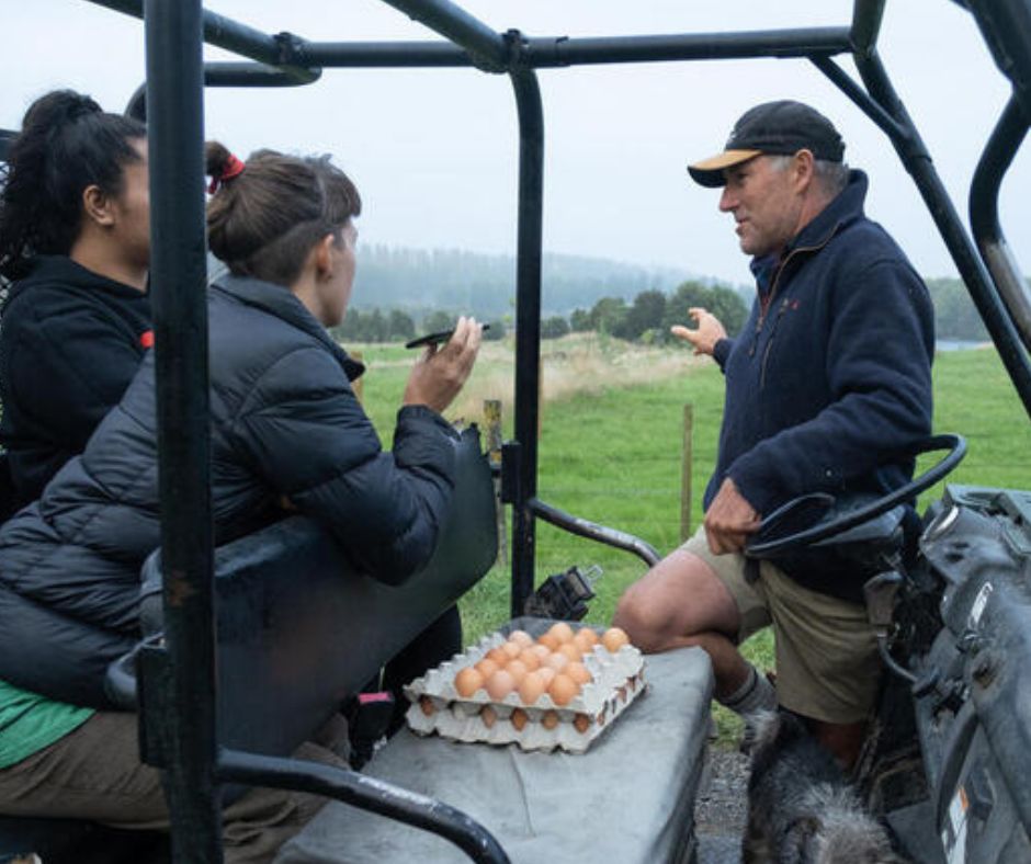 Three people are talking outside, leanin on a quad bike, a tray of eggs between them