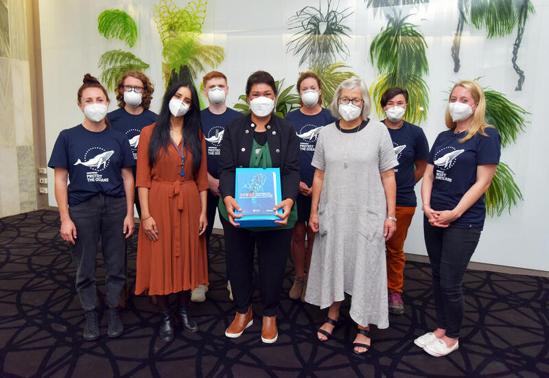 A group of people in blue tshirts with three politicians in front, one holding a blue folder.