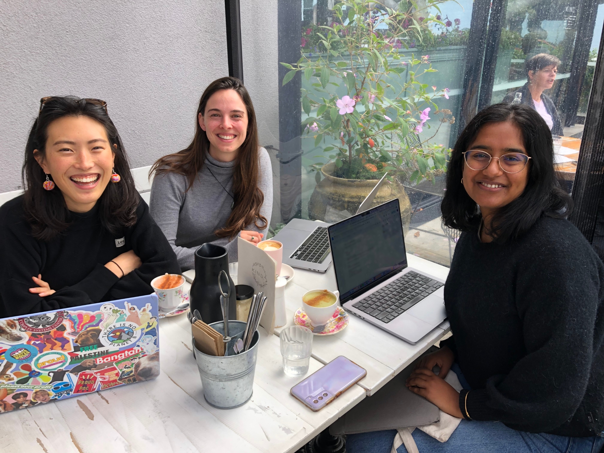 Three people smiling at a cafe table with laptops