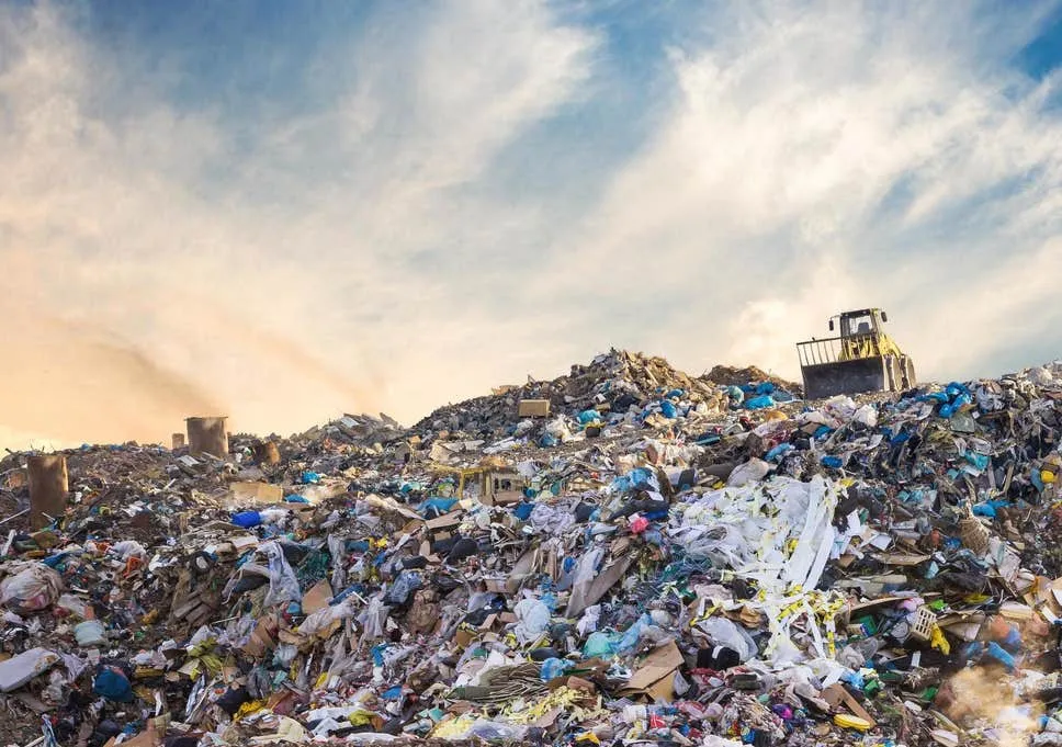 A pile of clothes in a landfill, a tractor is small at top