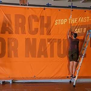 Greenpeace staff paint a March For Nature banner in the Greenpeace warehouse