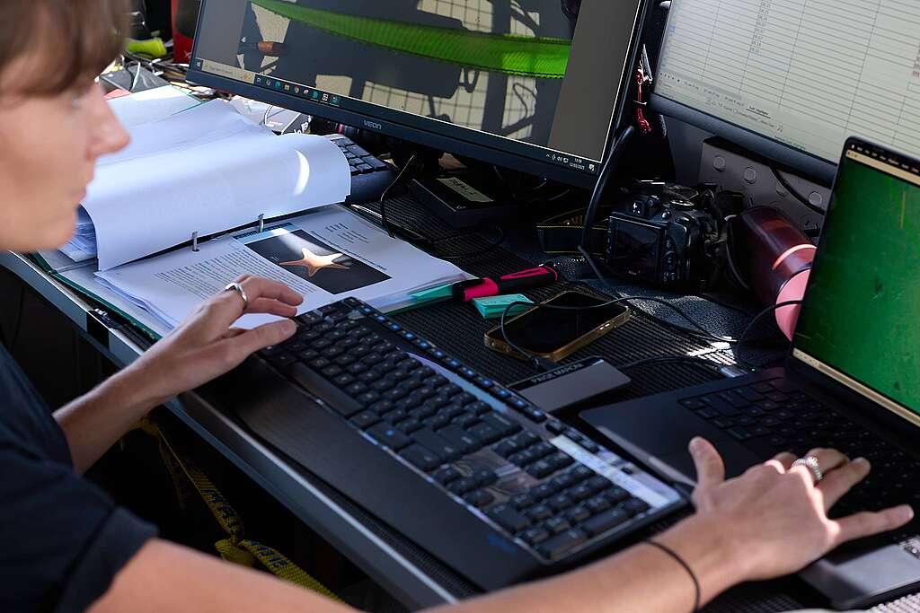 Scientist, Paige Maroni sitting with a keyboard in front of her and a laptop, reviews underwater camera footage