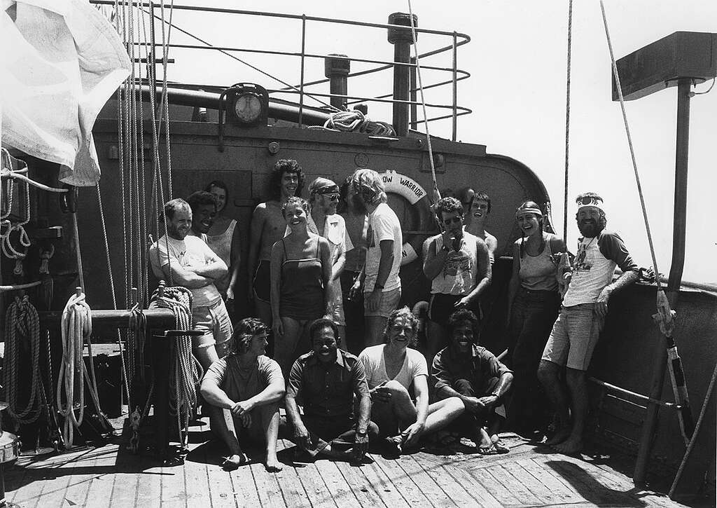 An old black and white photograph of the crew sitting together on the deck of the Rainbow Warrior
