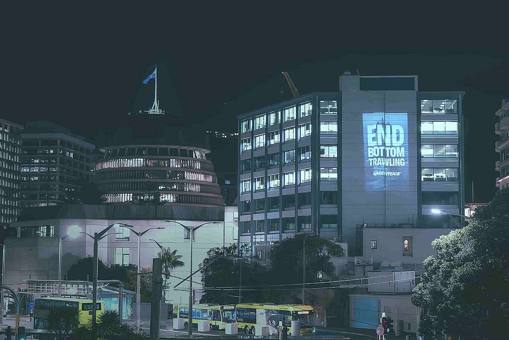 A projection reading End Bottom Trawling is projected onto a building in downtown Wellington with the Beehive in the shot