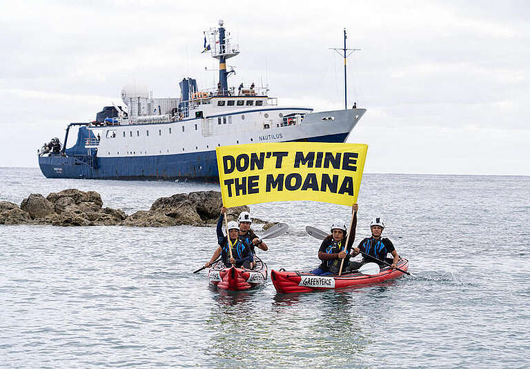 Cook Island activists in kayaks hold a banner reading "Don't Mine the Moana" in front of a ship that is returning to port in Rarotonga after conducting research that could be used to fast track seabed mining