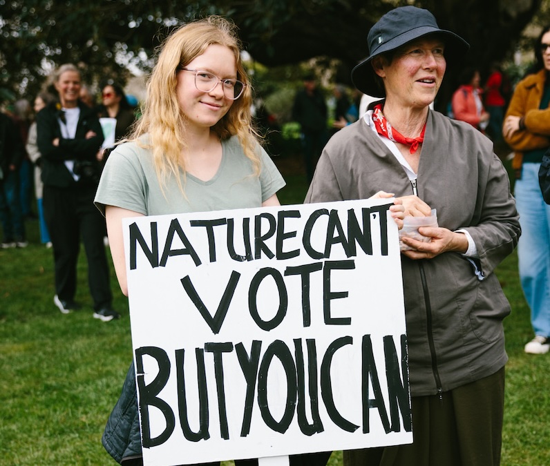 Two people hold a home made sign that says NATURE CAN'T VOTE BUT YOU CAN