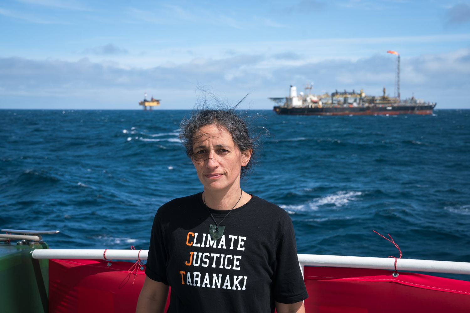 Climate Justice Taranaki member Emily Bailey on the Greenpeace ship Rainbow Warrior with OMV-owned oil drilling platform and oil processing ship in 2018