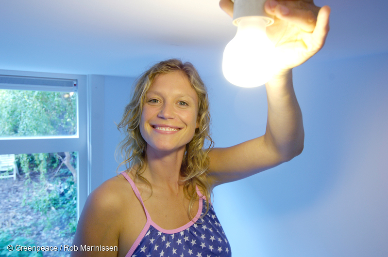 Mujer tomando con su mano una lámpara de bajo consumo encendida.