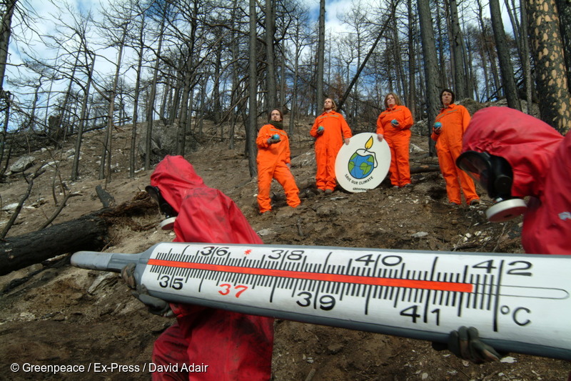 Activistas sostienen un gran termómetro y un cartel que dice "Salvemos nuestro clima" en el lugar de un incendio forestal para manifestarse contra los impactos del cambio climático.