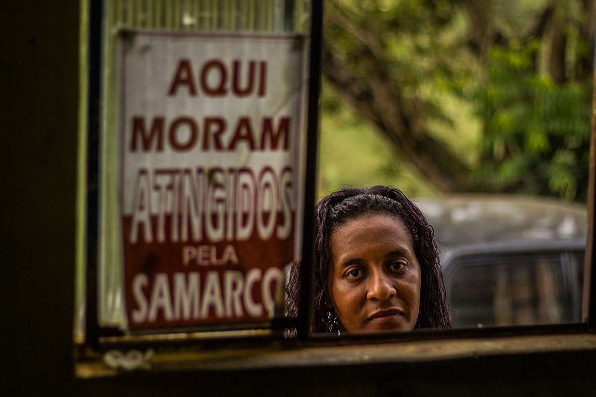 Simone Silva ao lado de placa que diz "Aqui moram atingidos pela Samarco"