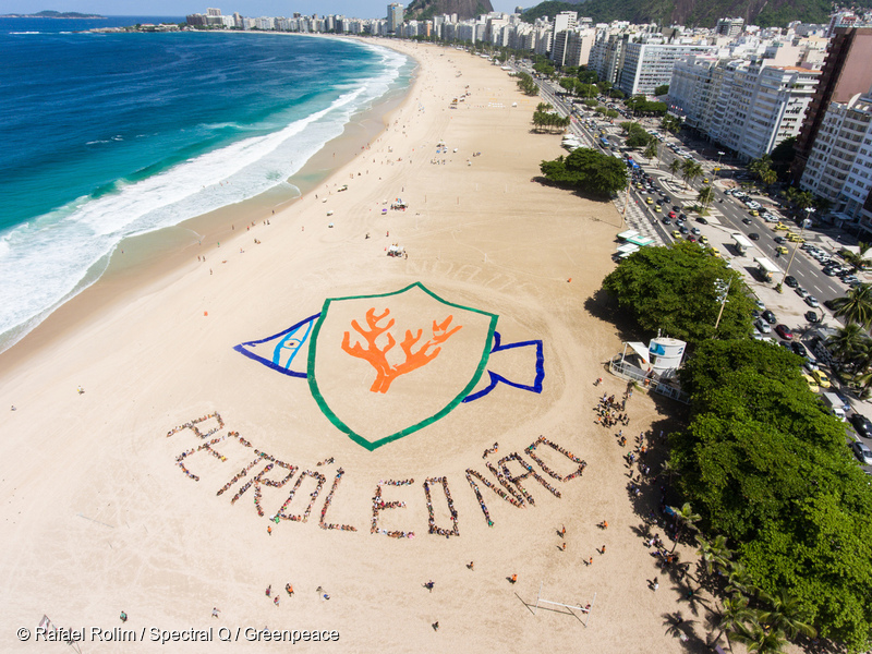 Frase "petróleo não" formada na praia por 500 pessoas. Em cima, o desenho de um peixe formado por tecidos