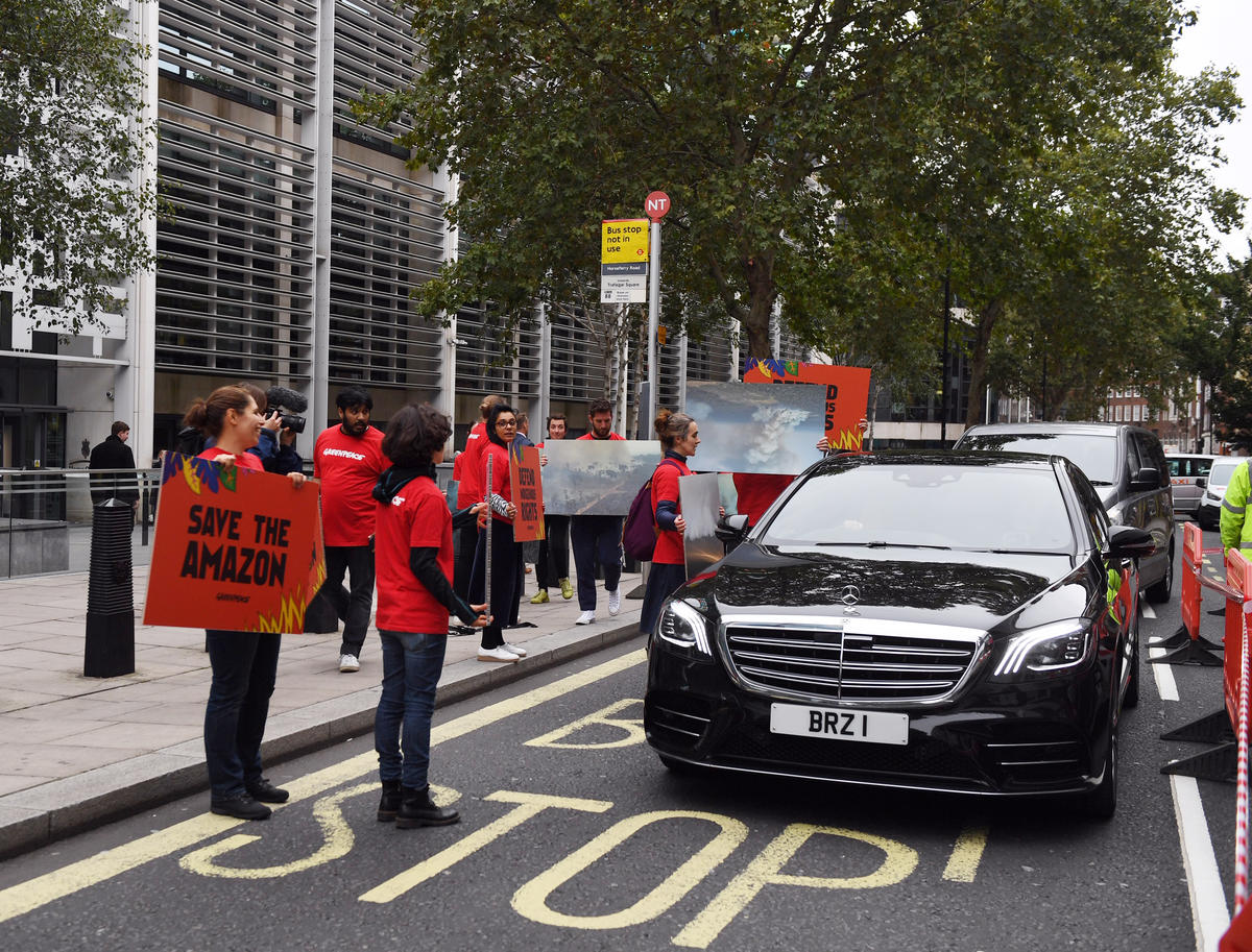 Carro oficial do Brasil chega ao prédio do escritório da ministra do meio ambiente do Reino Unido, em Londres, enquanto ativistas do Greenpeace exibem cartazes em protesto a favor da Amazônia