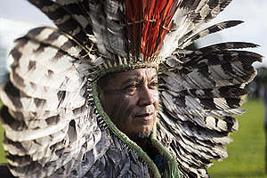 Indígena Kretã Kaingang com cocar de penas vermelhas e preto e brancas, sob a luz do sol em Brasília