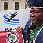 Com pintura vermelha e cocar azul, Alberto Terena segura cartaz com a logo da Articulação dos Povos Indívenas do Brasil - Apib
