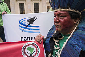 Com pintura vermelha e cocar azul, Alberto Terena segura cartaz com a logo da Articulação dos Povos Indívenas do Brasil - Apib