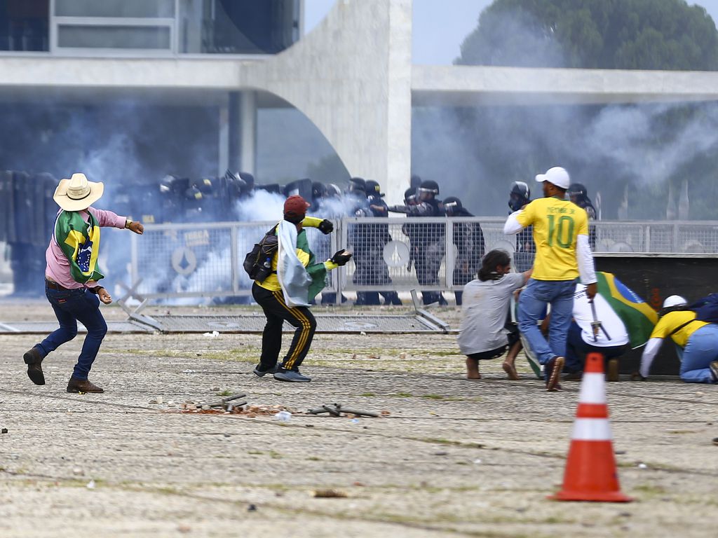 Homens vestidos com a camiseta do Brasil jogam pedras em direção ao Palácio do Planalto, em Brasília