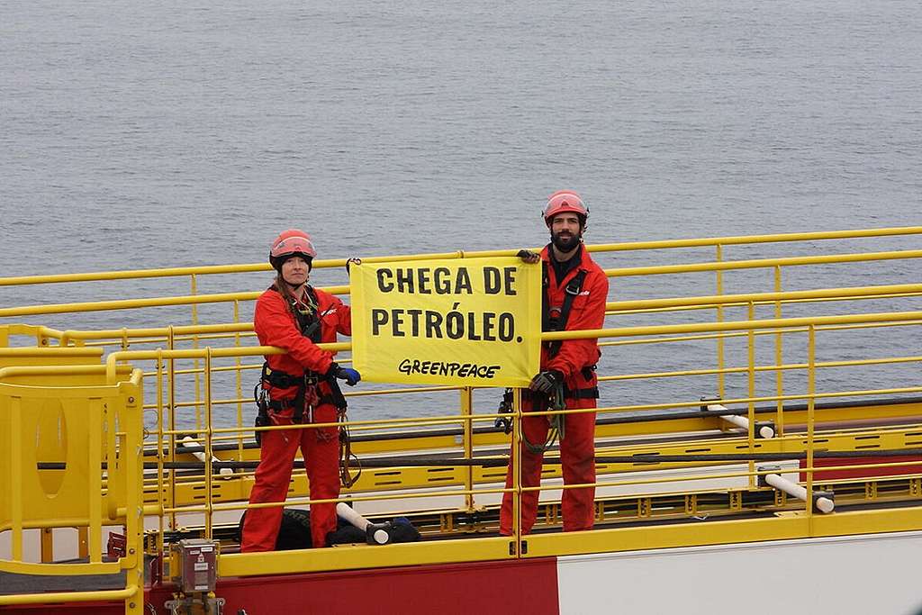 Ativistas que ocupam plataforma da Shell erguem banner com a mensagem "Chega de Petróleo", em português 