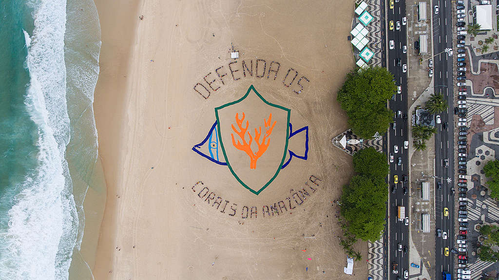 Uma imagem aérea da orla de Copacabana, no Rio de Janeiro, com a mensagem "Defenda os Corais da Amazônia" escrita na areia.