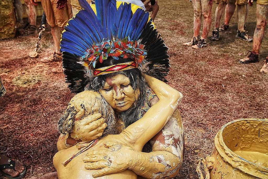Indígenas pintadas com tinta dourada simulando o ouro do garimpo ilegal, abraçadas durante protesto em Brasília