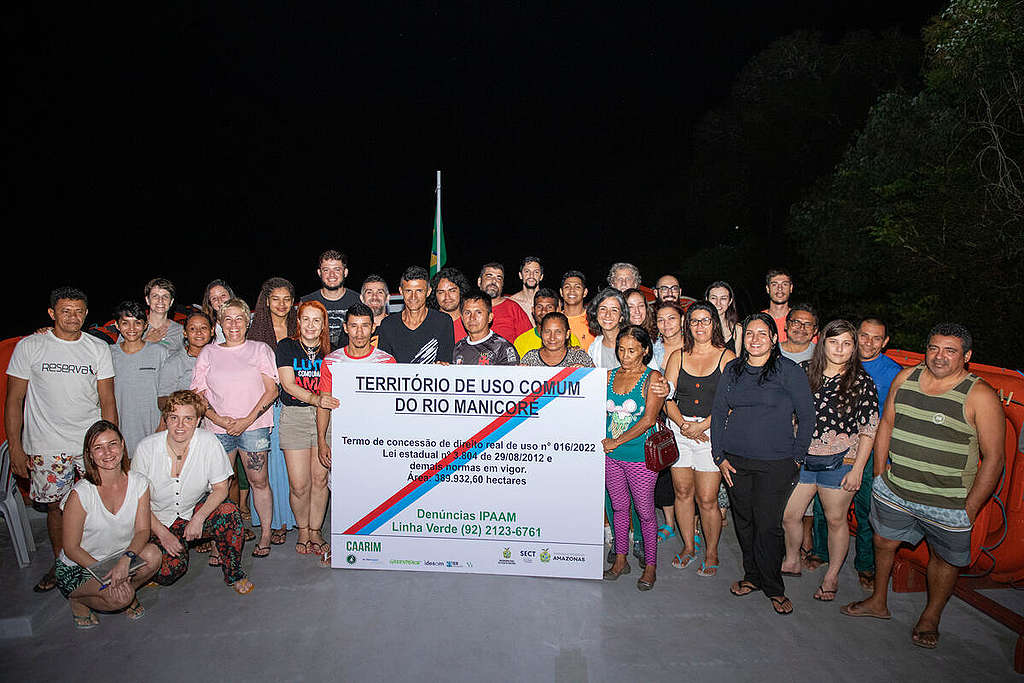 Pessoas aglomeradas segurando uma placa sobre a demarcação do território das comunidades ribeirinhas do Rio Manicoré; integrantes do Greenpeace ao lado de pessoas das comunidades locais, durante a expedição "Amazônia que precisamos", realizada em 2022