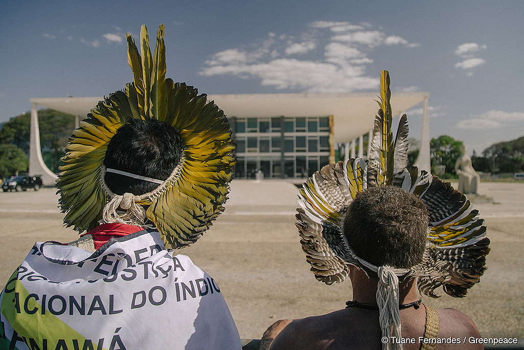 Foto mostrando 2 pessoas indígenas de costas olhando para o prédio do Supremo Tribunal Federal.