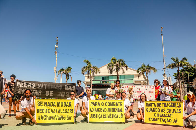 Pessoas segurando banners em recife com dizeres "pelas vítimas das chuvas de 2022"