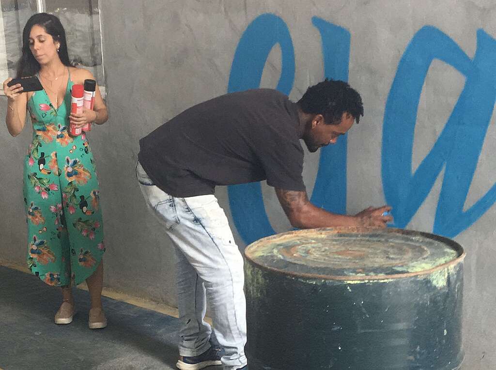 Foto de duas pessoas voluntárias. Uma delas desenha grafite na parede.