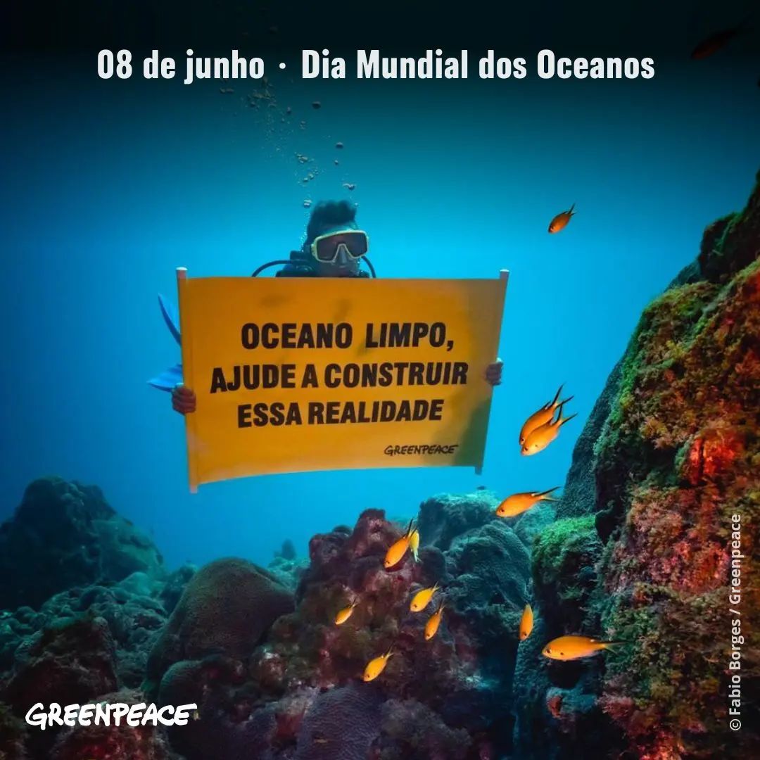 Ativista vestindo um traje de mergulho, submerso na água, segurando um banner com o texto: 'Oceano limpo, ajude a construir essa realidade', acompanhado do logotipo do Greenpeace