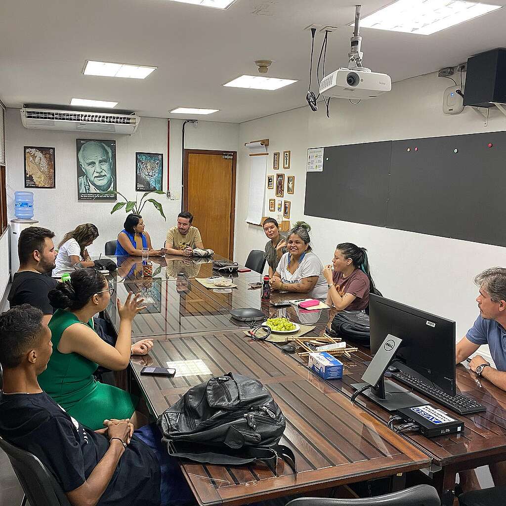 Pessoas voluntárias sentadas ao redor de mesa, em uma conversa.