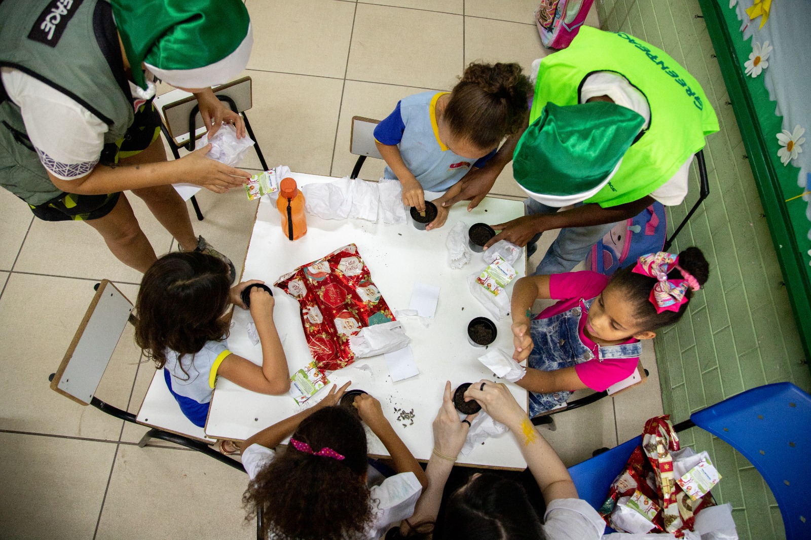 Fotografia de voluntários do Greenpeace realizando o plantio de sementinhas junto a algumas crianças do ensino infantil.