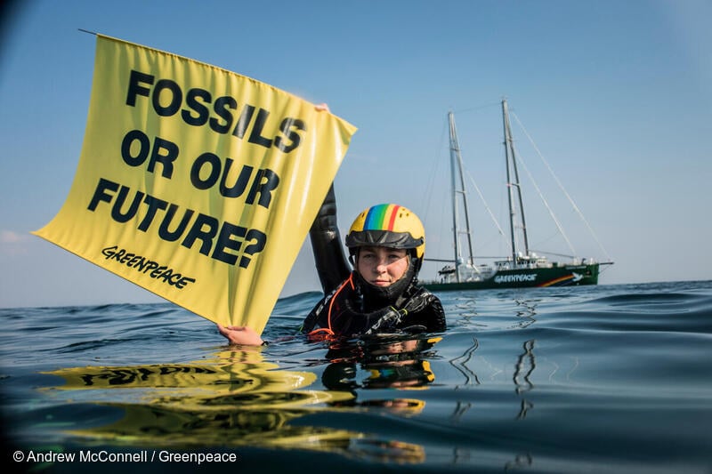 Danish activist Ida Marie in the water with hand banner reading "Fossils our our future".