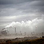 A thick layer of smog hovers above the ground while smoke continues to pour out of the smoke stacks at the oil refinery.