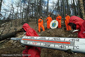 Activistas sostienen un gran termómetro y un cartel que dice "Salvemos nuestro clima" en el lugar de un incendio forestal para manifestarse contra los impactos del cambio climático.