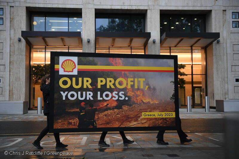 Cartel que muestra una imagen de un bombero griego luchando para contener un incendio forestal cerca de Atenas, está adornado con el logotipo de Shell y presenta el lema "Nuestras ganancias, su pérdida"