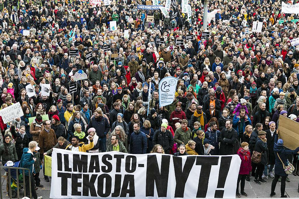 Tuhansien ihmisten väkijoukko ilmastomarssilla 2018. Etualalla ihmiset pitävät banneria jossa lukee: ilmastotekoja nyt!