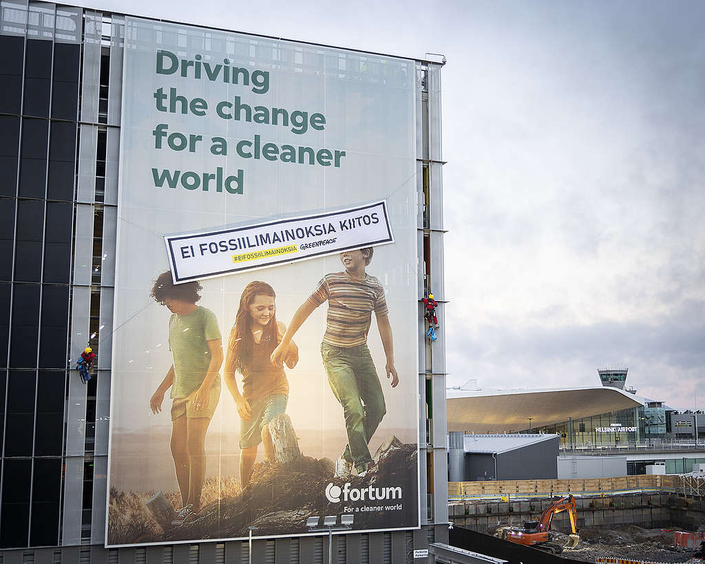 Fortumin mainos Helsinki-Vantaan lentoasemalla, jossa lukee "Driving the change for a cleaner world". Mainoksen päällä on Greenpeacen banderolli tekstillä "Ei fossiilimainoksia, kiitos".