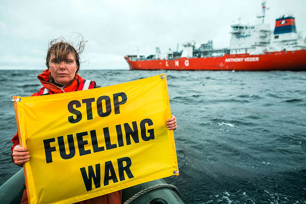 Aktivisti pitelee veneessä LNG-laivan edessä banderollia, jossa teksti "Stop fuelling war". Aktivisti kumiveneessä LNG-aluksen edessä Torniossa. Aktivistin kädessä on kyltti, jossa lukee "STOP FUELLING WAR".