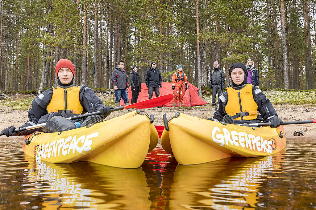 Aktivisteja, joista kaksi ovat kajakeissa rantavedessä, ja loput rannalla, Oulujärven saarella puolustamassa hakkuu-uhan alla ollutta metsää. Kahdeksan aktivistia järven rannalla, joista kaksi on kajakeissa rantavedessä.