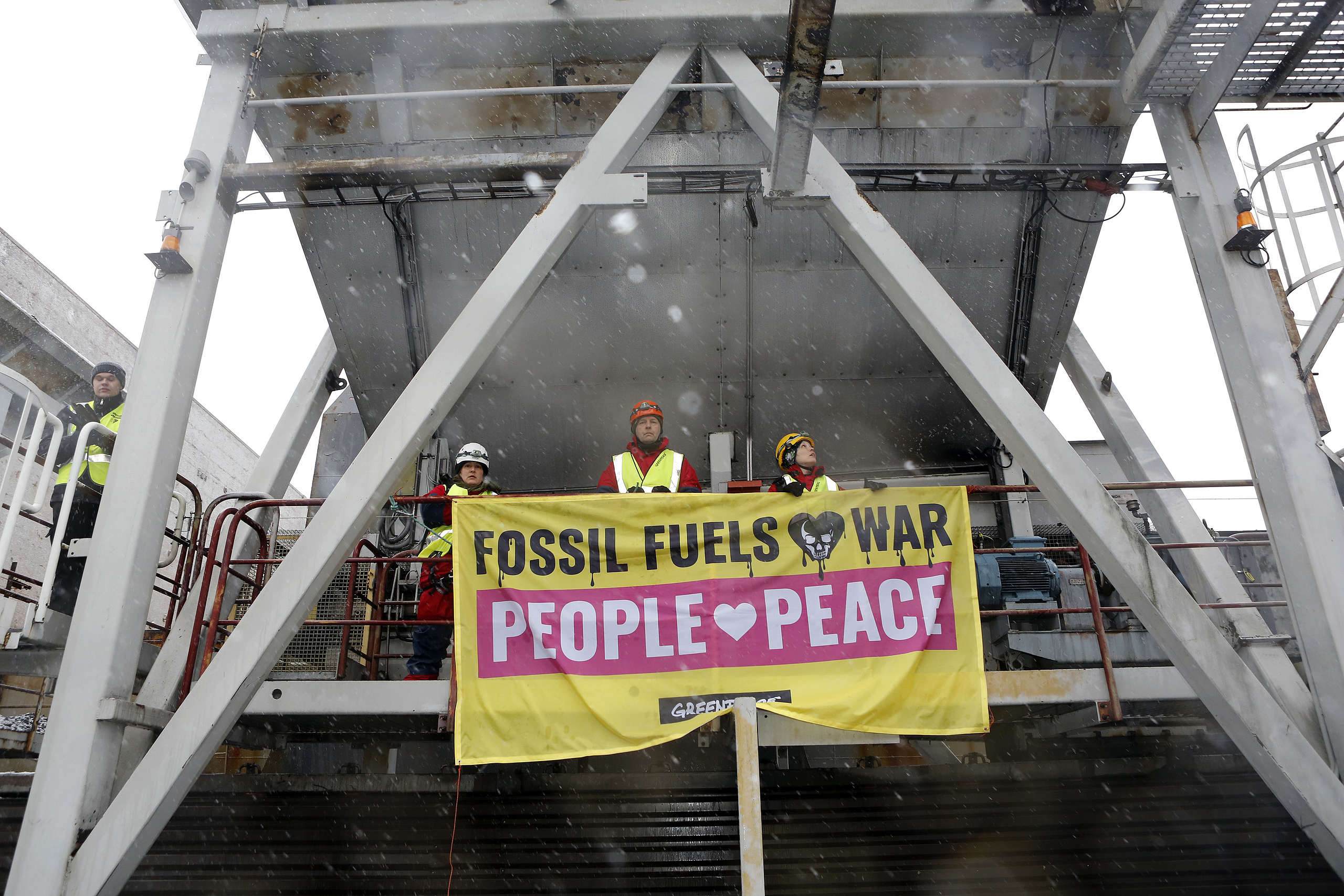 Aktivisteja satamassa estämässä hiilen tuotia Helsinkiin. Aktivisteilla on banderolli, jossa lukee "Fossil fuels love war" ja "people love peace".