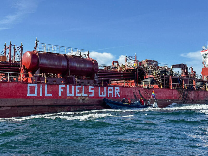 Vene punaisen laivan vierellä, jonka kyljessä lukee "Oil Fuels War".